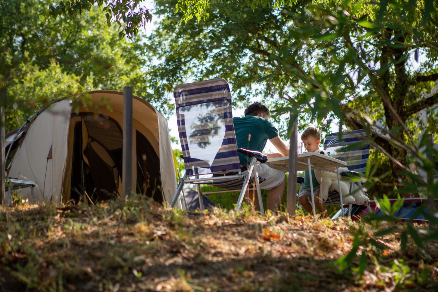Vader en zoon aan tafel bij hun tent op een schaduwrijke plek